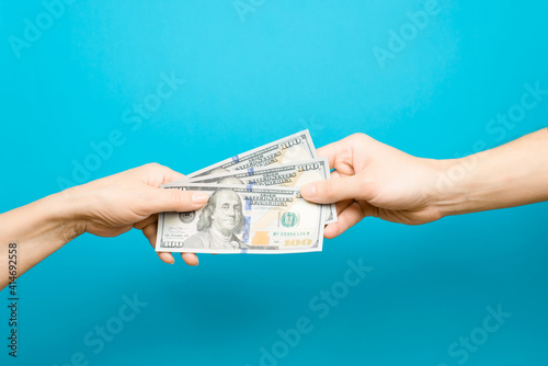 Hand giving one hundred dollar bills and hand taking money, blue background. The concept of salary, loan, credit, money circulation