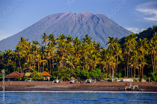 Agung volcano in Bali Indonesia from the sea with palm trees and fisherman boats 