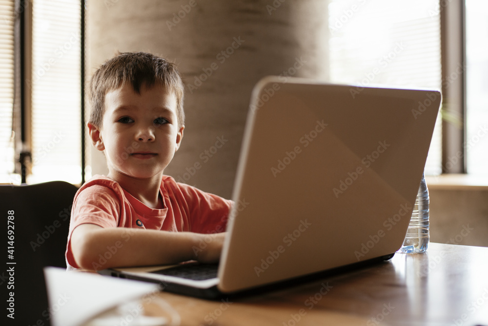 Portrait of cute smiling little boy sitting on office chair behind desk in the office. Happy boy using laptop. Portrait of cute smiling little boy sitting on office chair behind desk in the office. Happy boy using laptop.