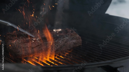 Roasting juicy meat rack focus pastrami steak in burning charcoals fire on bbq grid, flames and smoke in slow motion. Barbecue grill outside in winter