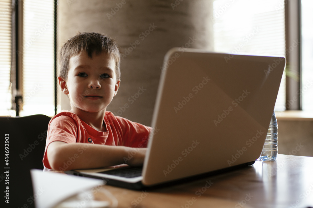Portrait of cute smiling little boy sitting on office chair behind desk in the office. Happy boy using laptop. Portrait of cute smiling little boy sitting on office chair behind desk in the office. Happy boy using laptop.