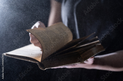 Hands hold Vintage open Book Glows on black background. Concept of mystery, riddle and secret 