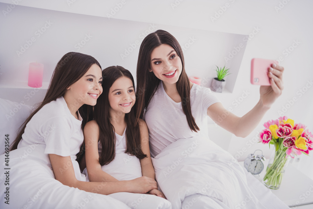 Photo of charming pretty three sisters sleepwear sitting bed having rest tacking selfie modern gadget inside indoors home room Photo of charming pretty three sisters sleepwear sitting bed having rest tacking selfie modern gadget inside indoors home room