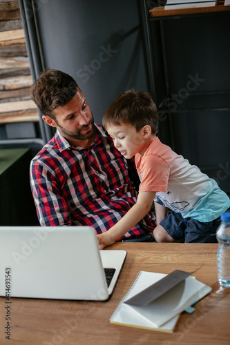 Young businessman with his son in the office. Father working on laptop while babysitting his son.
