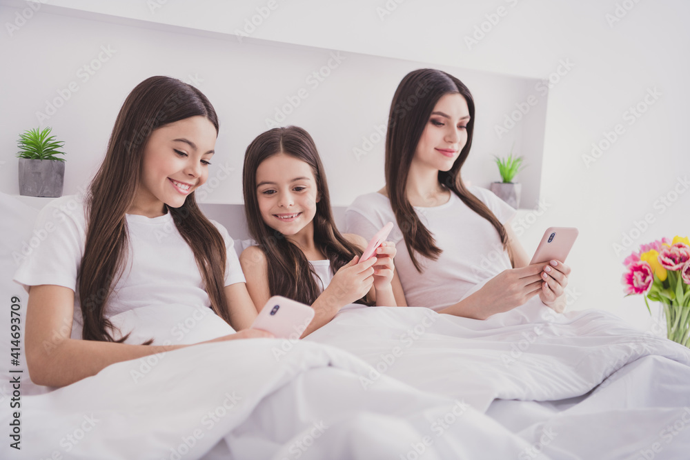 Photo of shiny charming three sisters sleepwear sitting bed having rest typing modern gadgets inside indoors home room Photo of shiny charming three sisters sleepwear sitting bed having rest typing modern gadgets inside indoors home room