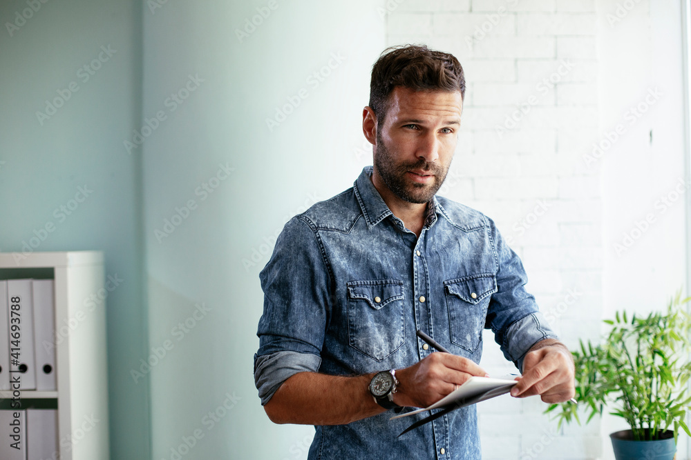 Fototapeta premium Handsome businessman sitting on a desk, writing notes. Businessman making businessplan..