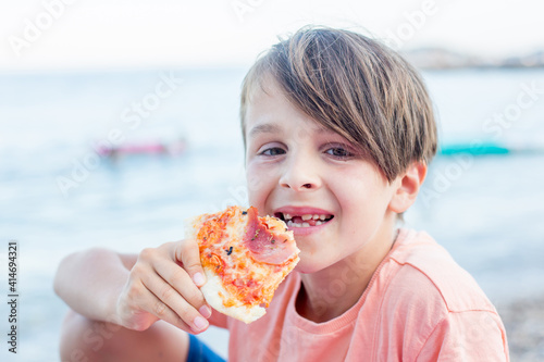 Sweet toddler child, eating pizza on the beach, having fun, smiling happily, kid enjoying dinner