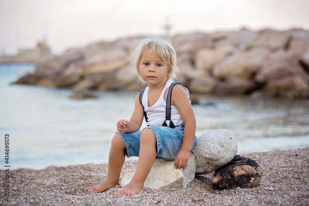 Blond toddler child, boy, playing on the beach in the evening Blond toddler child, boy, playing on the beach in the evening