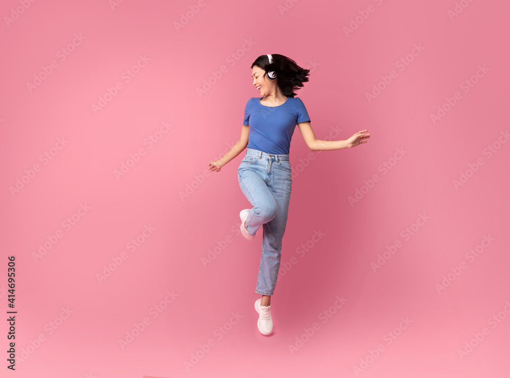 Smiling Young Asian Woman Jumping Listening To Music