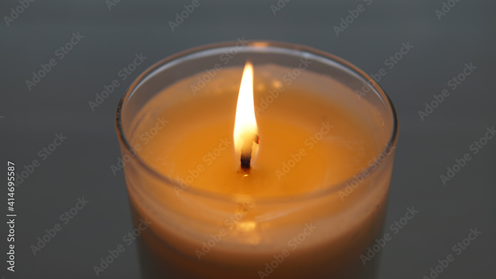 close view of lit candle with a textured white and gray blurred background close view of lit candle with a textured white and gray blurred background
