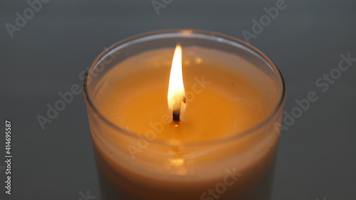close view of lit candle with a textured white and gray blurred background 