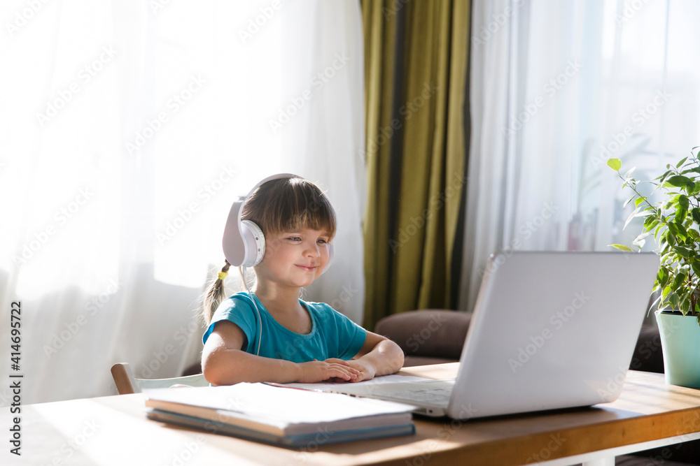 child girl in headphones is using a laptop and study online with video call teacher at home. homeschooling, distant learning child girl in headphones is using a laptop and study online with video call teacher at home. homeschooling, distant learning