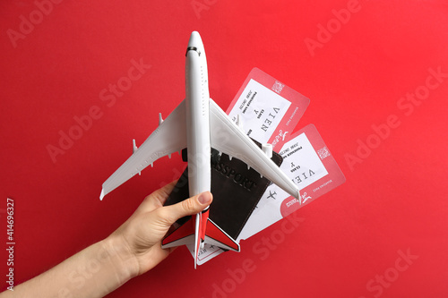 Woman holding toy airplane, passport and tickets on red background, closeup