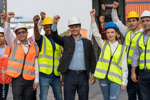 A group of employees and management team wearing logistic uniforms for exporting products abroad, stand to raise their hands together to manage at the container yard until they are successful.