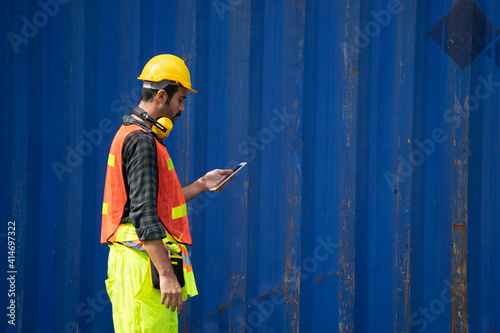 Caucasian worker in safety vest reflective with Safety helmet holding tablet and talking to radio reciever to checked about his work