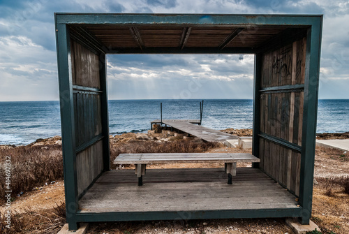 View through a roofed bench on the rocky beach and the sea in Paphos Cyprus at a cloudy weather after rain
