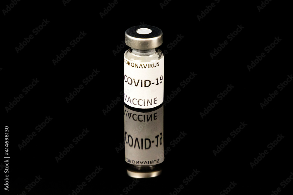 Coronavirus Covid 19 vaccine concept. Small glass bottle with silver cap and label on black background Coronavirus Covid 19 vaccine concept. Small glass bottle with silver cap and label on black background
