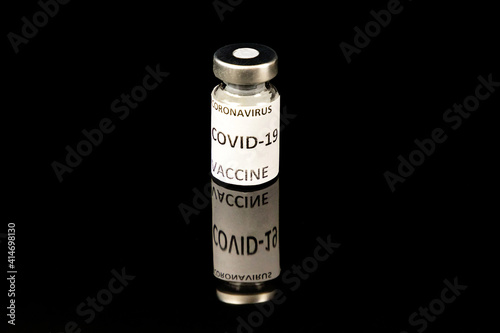 Coronavirus Covid 19 vaccine concept. Small glass bottle with silver cap and label on black background