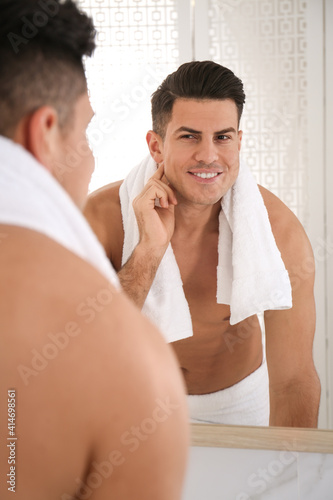 Handsome man with towel near mirror in bathroom