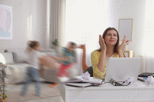 Children disturbing overwhelmed woman in living room. Working from home during quarantine photo