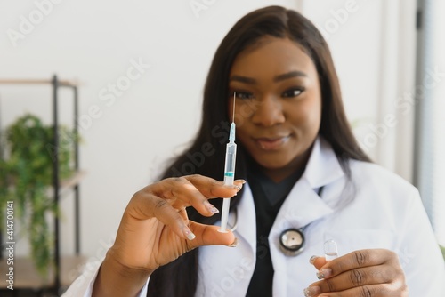 healthcare and medical concept - african doctor holding syringe with injection