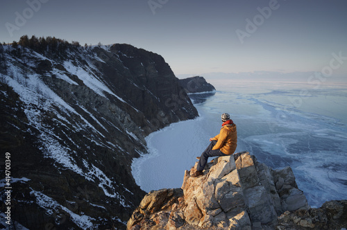 Man Sitting on Edge of Cliff and Looking on Frozen Lake Baikal in Winter. Olkhon Island, Siberia, Russia.