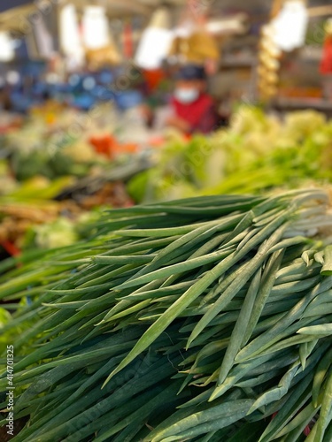 Traditional Market and Gourmet Experience in Asia, close up for a bunch of green onion in traditional market, there are some fruit behind