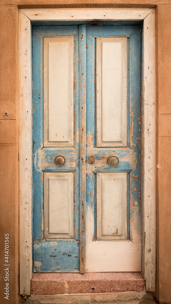 Wooden doors with blue and white weathered pealing paint and with two copper doorknobs on Kythira, Greece