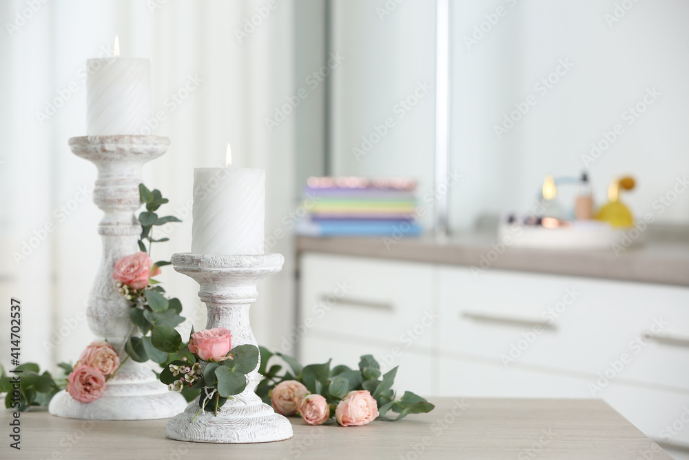 Vintage candlesticks with burning candles, roses and eucalyptus on table in room. Space for text