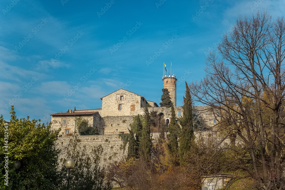 Part of the castle of the city of Brescia on a sunny winter day. A view from the park. Castello di Brescia, Lombardy, Italy. Medieval castle with battlements, a tower, drawbridge and ramparts. 