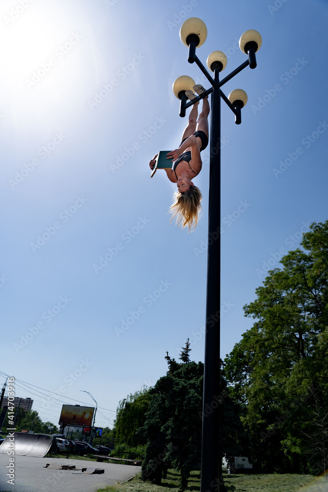 Girl hanging by feet upside down in the street on the Street light and reading book. Concept of combined knowledge, education and sport in the same time 