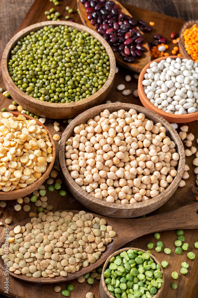 Different legumes. Mung beans, red beans, lentils, peas and chickpeas in wooden bowls on a brown wooden kitchen table. Beans close-up. Vegetarian food