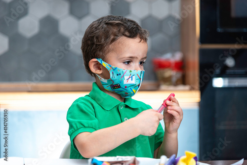 Boy's in a mask is doing homework. Boy's in a mask is drawing.