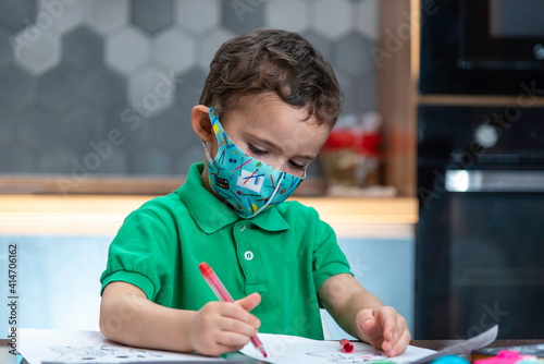 Boy's in a mask is doing homework. Boy's in a mask is drawing.