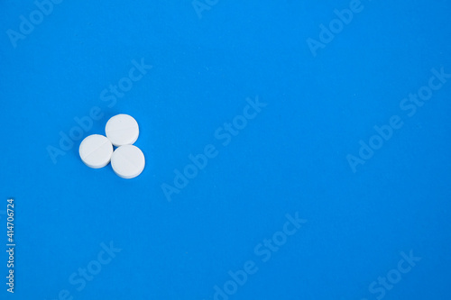 Three round white pills, vitamins on a blue background, place for text. Concept of medicines, healthcare, immunity.