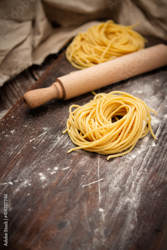 Uncooked fresh spaghetti nests on a wooden table with a rolling pin. Italian pasta homemade. Text space