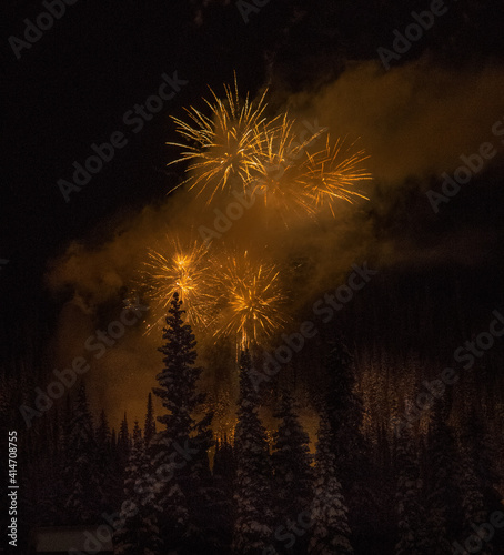 festive fireworks display in woods over tall trees at ski hill on new years eve celebrating a new year 