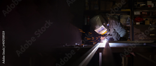 An adult male works in an old workshop. He holds a welding machine in his hand and welds the metal structure. Copy space. photo