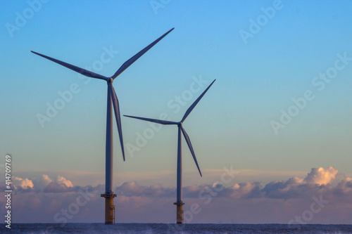 Two off shore wind turbines operating in calm conditions with dramatic sky in the distance