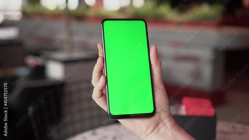 Close up of a woman's hand holding a mobile telephone with a vertical green screen in restaurant chroma key smartphone technology cell phone street touch message display hand Close up of a woman's hand holding a mobile telephone with a vertical green screen in restaurant chroma key smartphone technology cell phone street touch message display hand