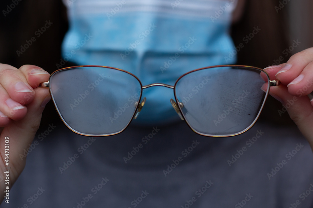 Closeup of a person in a protective mask holding foggy glasses.