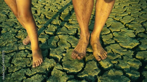child and adult walk barefoot on dry cracked mud ground of a lake that has dried up due to a drought from climate change and global warming

