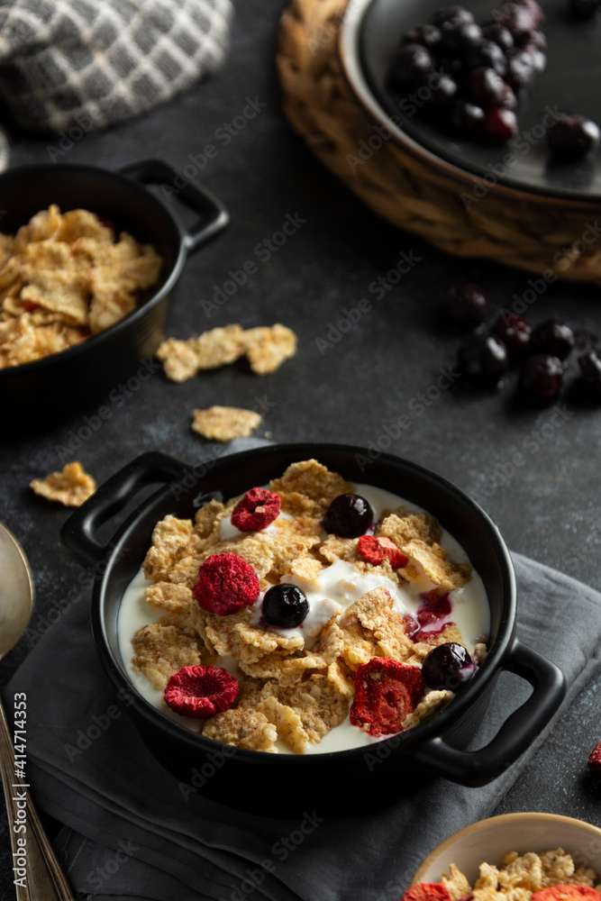 Corn flakes with strawberry and blueberry in black bowls over dark background, top view. Corn flakes with strawberry and blueberry in black bowls over dark background, top view.