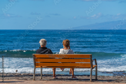 Backview of a Couple sitting on bench relaxing looking at ocean beach © ggfoto