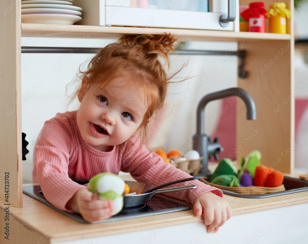cute toddler baby girl playing on toy kitchen at home - obrazy, fototapety, plakaty 