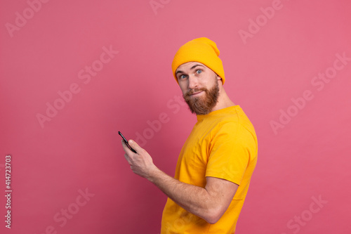 European handsome happy cheerful man with mobile phone smiling and look to camera pink background