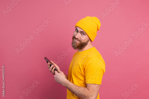 European handsome happy cheerful man with mobile phone smiling and look to camera pink background