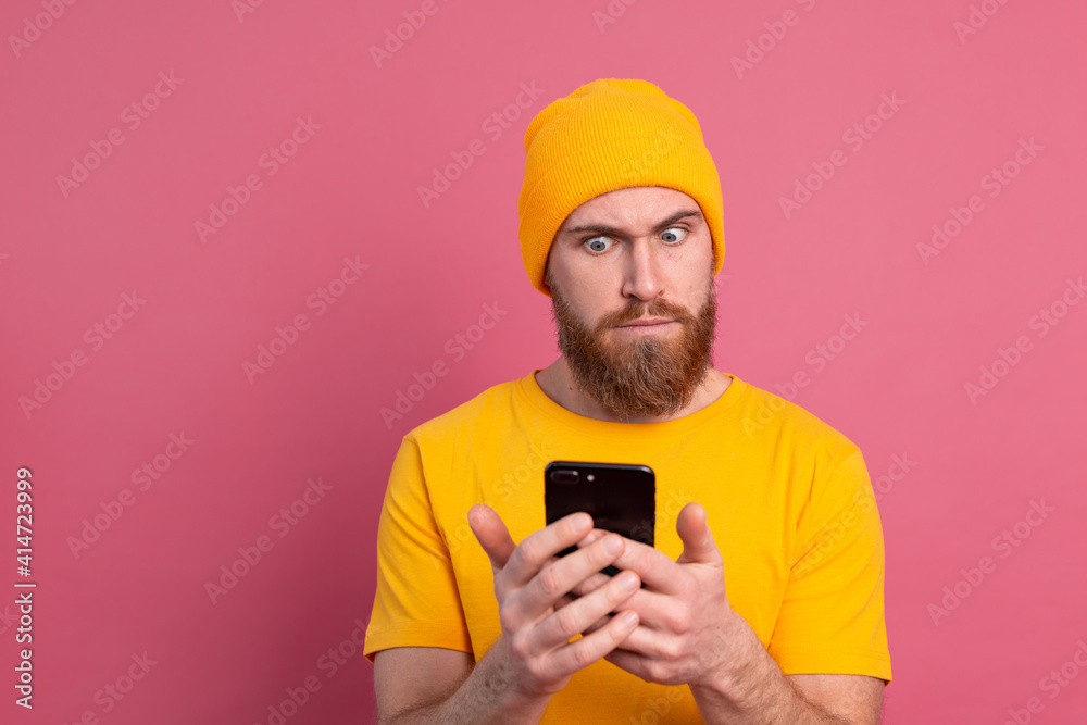 Portrait of concerned shocked mature bearded male gasping unhappy holding smartphone reading strange and disturbing message, isolated pink wall Portrait of concerned shocked mature bearded male gasping unhappy holding smartphone reading strange and disturbing message, isolated pink wall