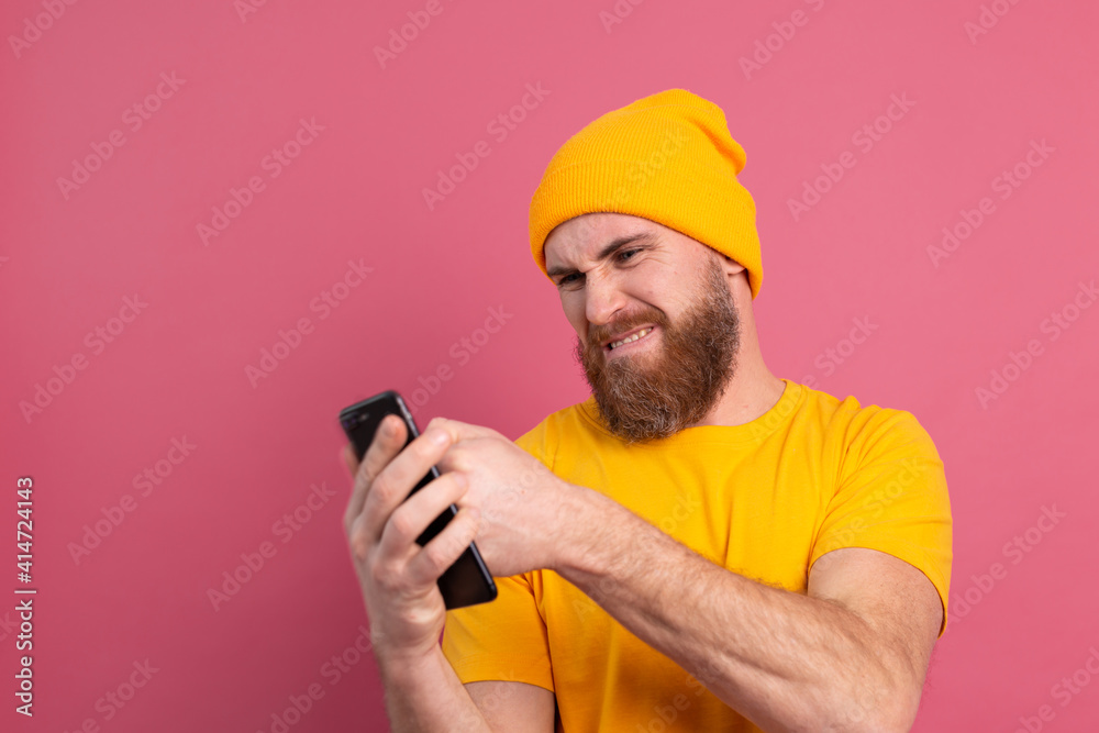 Angry european handsome man angry punching his mobile phone, pink background isolated Angry european handsome man angry punching his mobile phone, pink background isolated