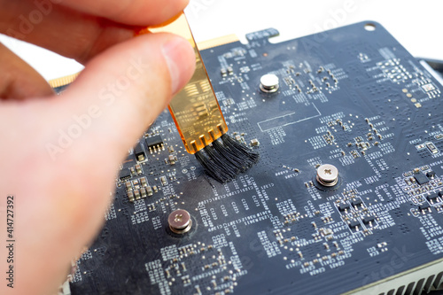 Close up of repairman cleaning dusty graphics card with brush on white table photo